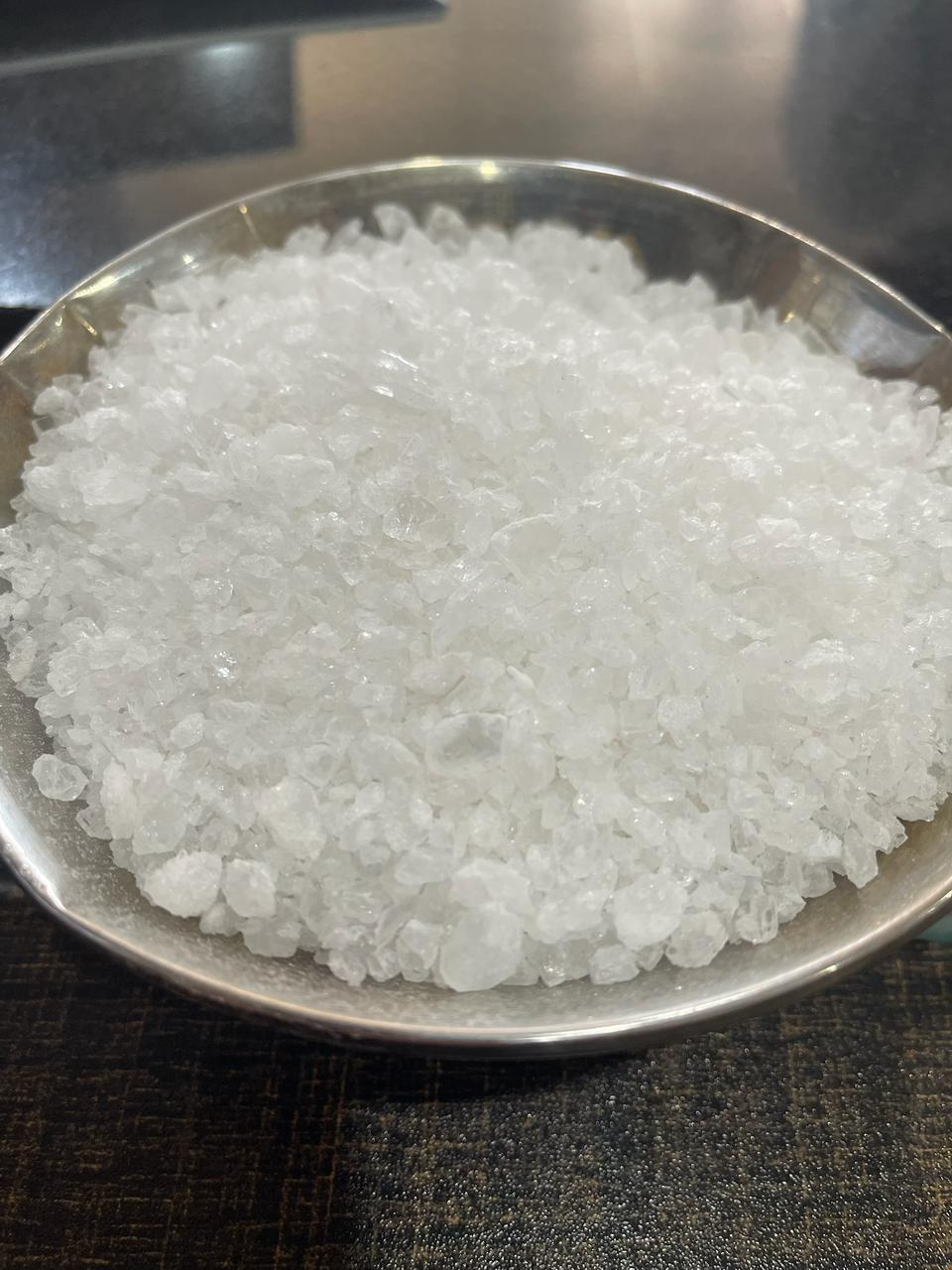 Metal bowl filled with large translucent and semi-opaque white salt crystals in coarse raw form